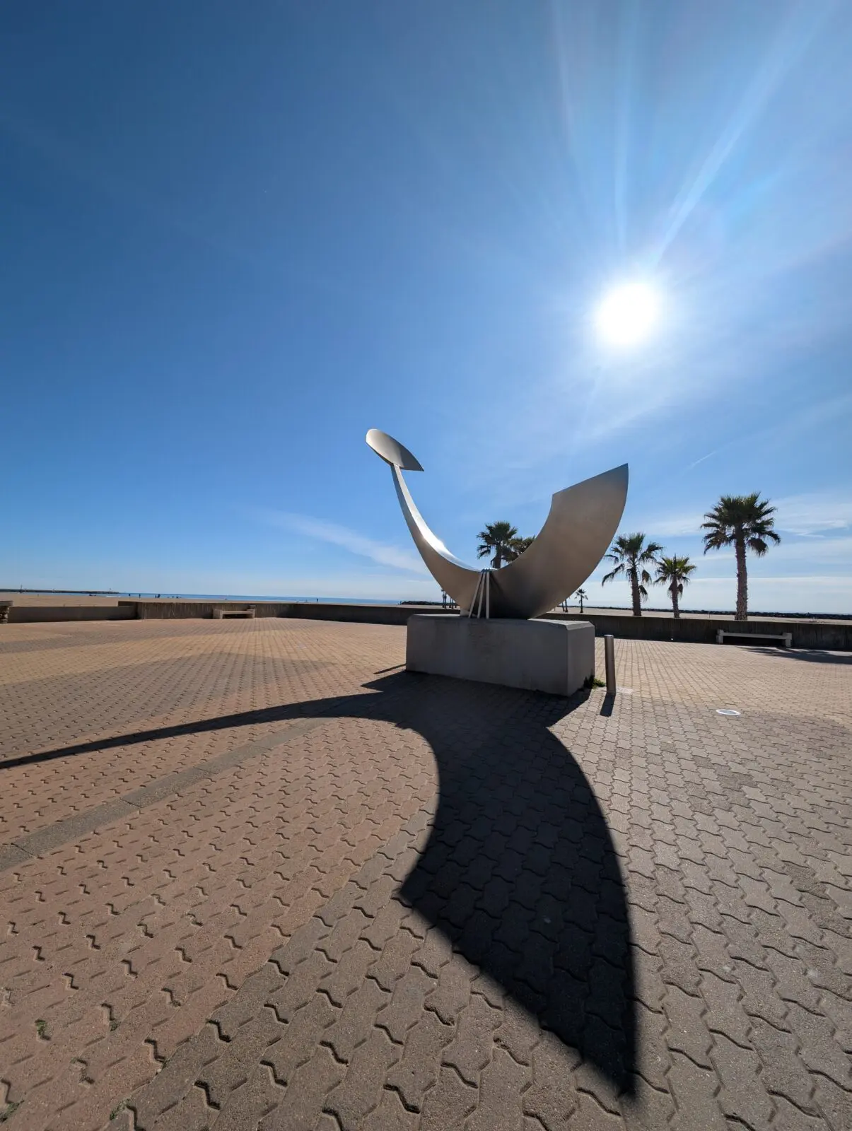 Statue en métal en forme de baleine avec palmiers sous ciel bleu et soleil