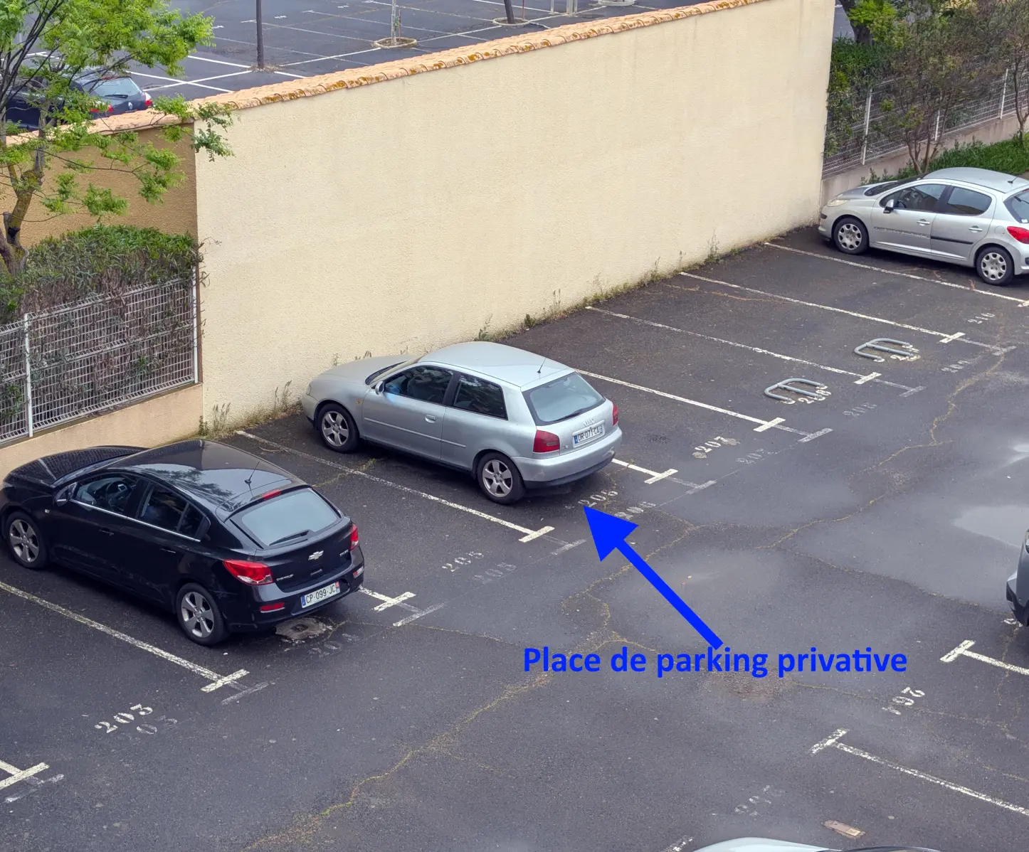 Emplacement de parking avec voiture grise stationnée contre mur beige